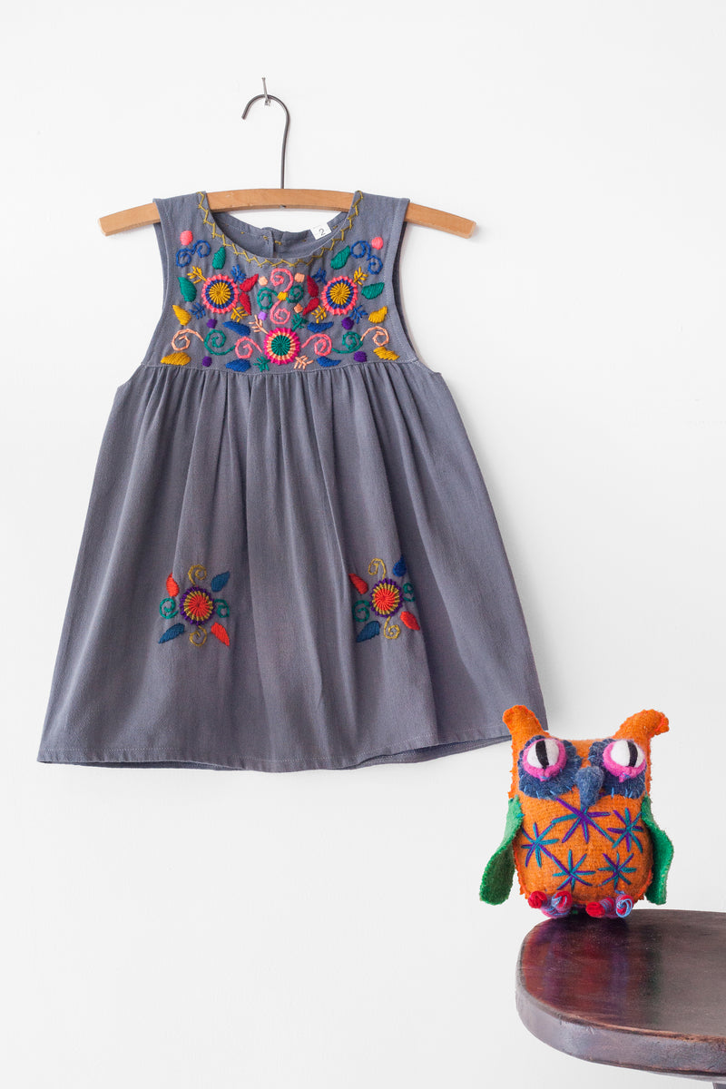 Kids sleeveless grey sun dress hanging with multicolor hand-embroidered floral pattern on chest and two hand-embroidered flowers near the bottom of the skirt on the front left and right.