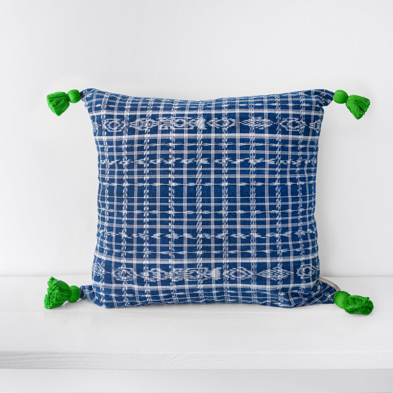 Large square blue and white pattern textile pillow with green tassels at each corner