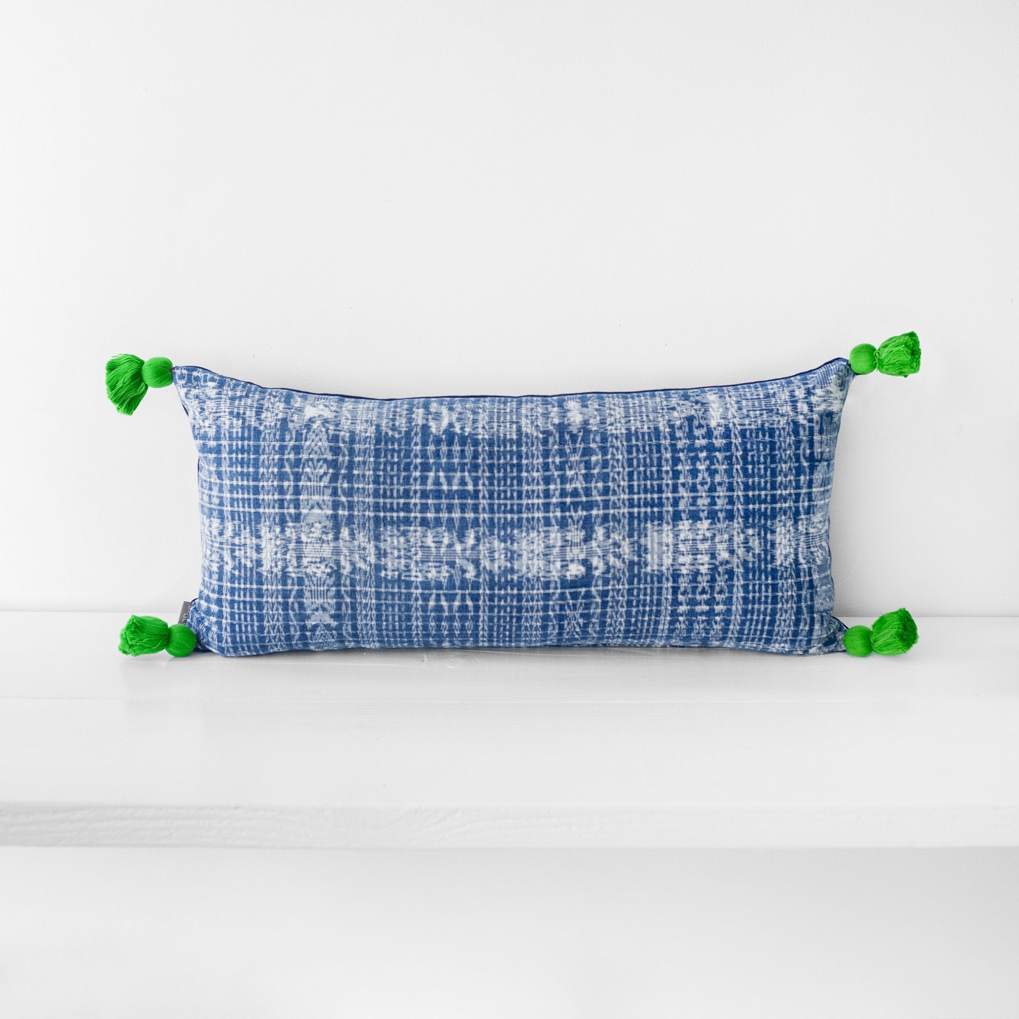 Large lumbar blue and white textile pillow with green tassels at each corner
