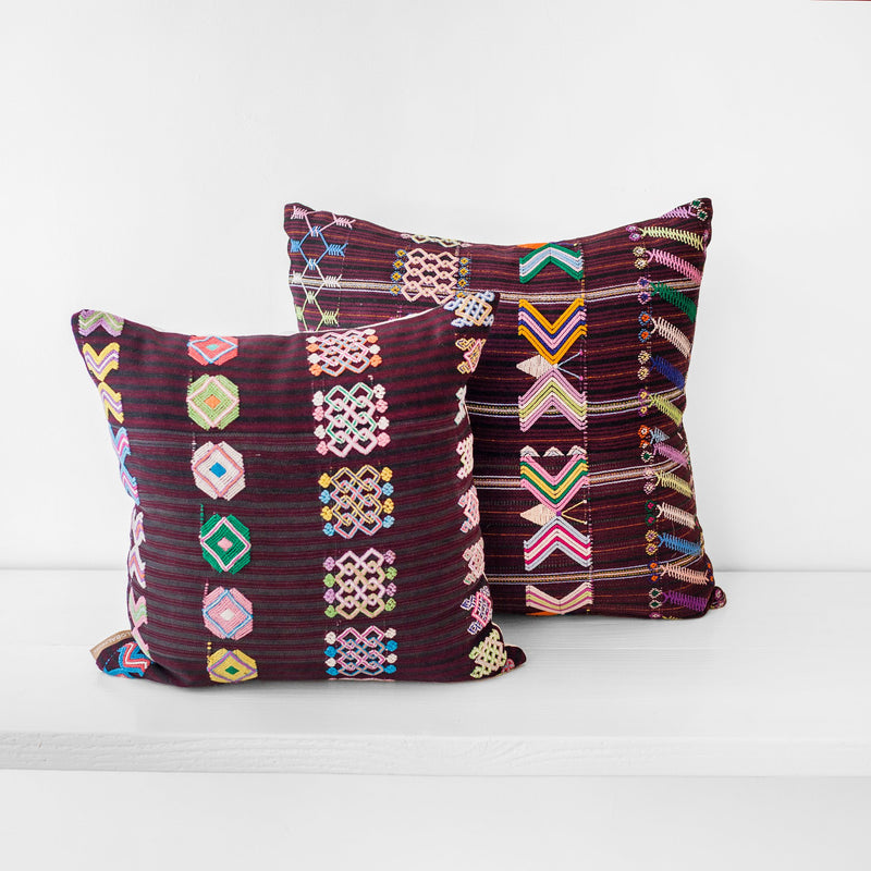 A pair of square throw pillows with a striped brown burgundy textile and colorful hand embroidered brocade
