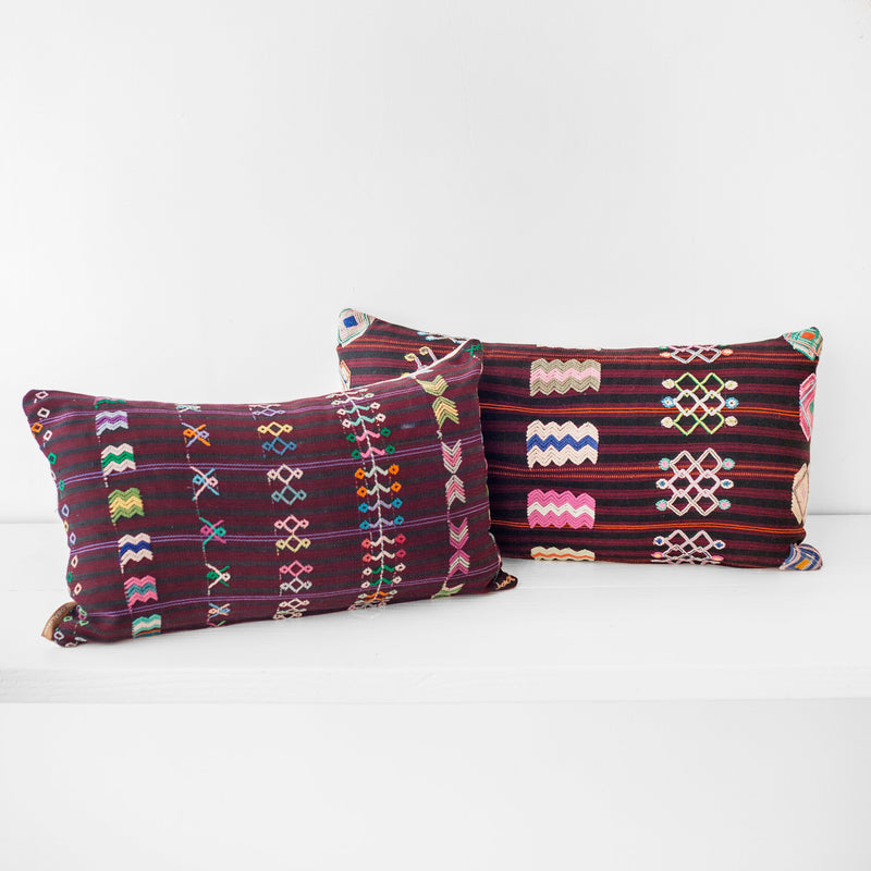 A pair of lumbar throw pillows with a striped brown burgundy textile and colorful hand embroidered brocade
