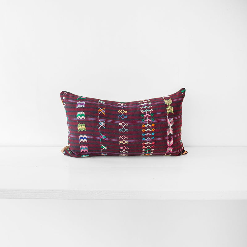 A lumbar throw pillow with a striped brown burgundy textile and colorful hand embroidered brocade