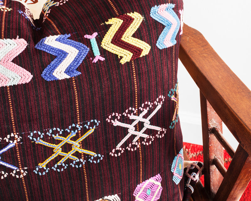 Detail of a throw pillow with colorful hand embroidered brocade on burgundy and black striped fabric