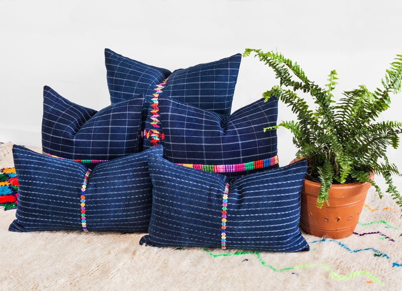 Collection of 5 lumbar and square pillows in varying shades of navy blue with white geometric lines and a colorful embroidered geometric seam running across