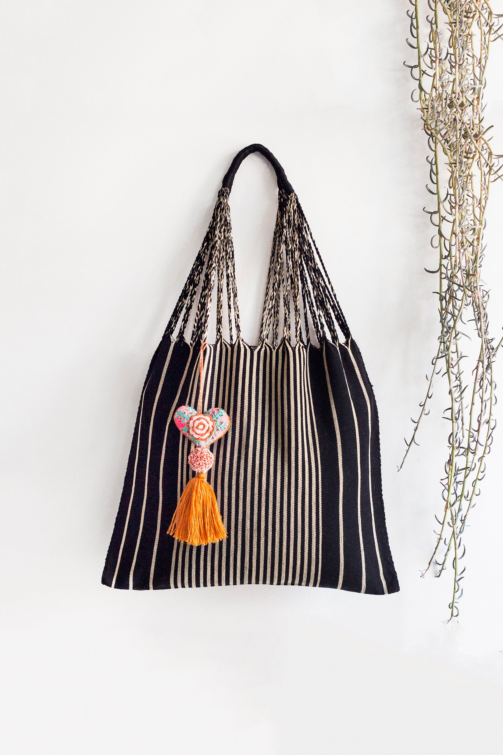 Woven black tote bag with vertical cream stripes and black and off-white braided straps attached to a curved black handle.