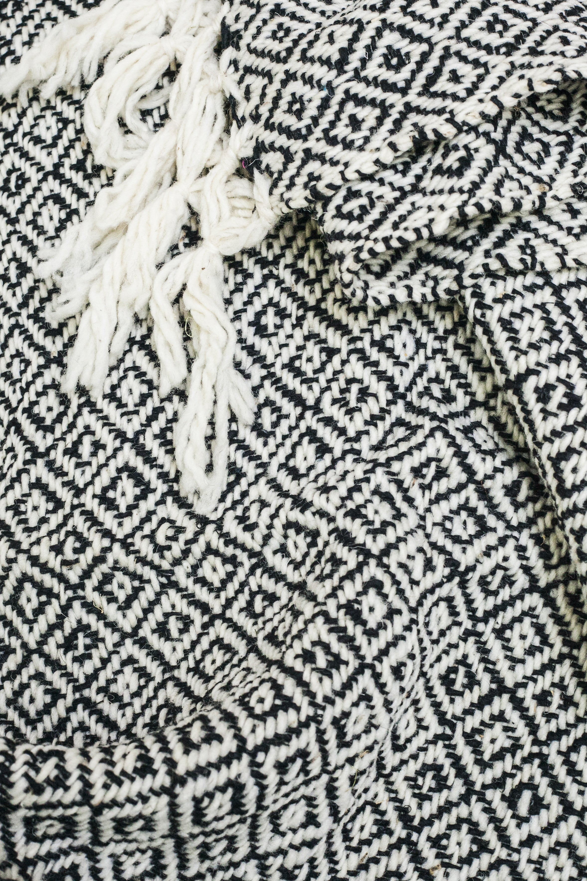 Detail of black and white diamond weaving and tied tassels from a wool throw blanket