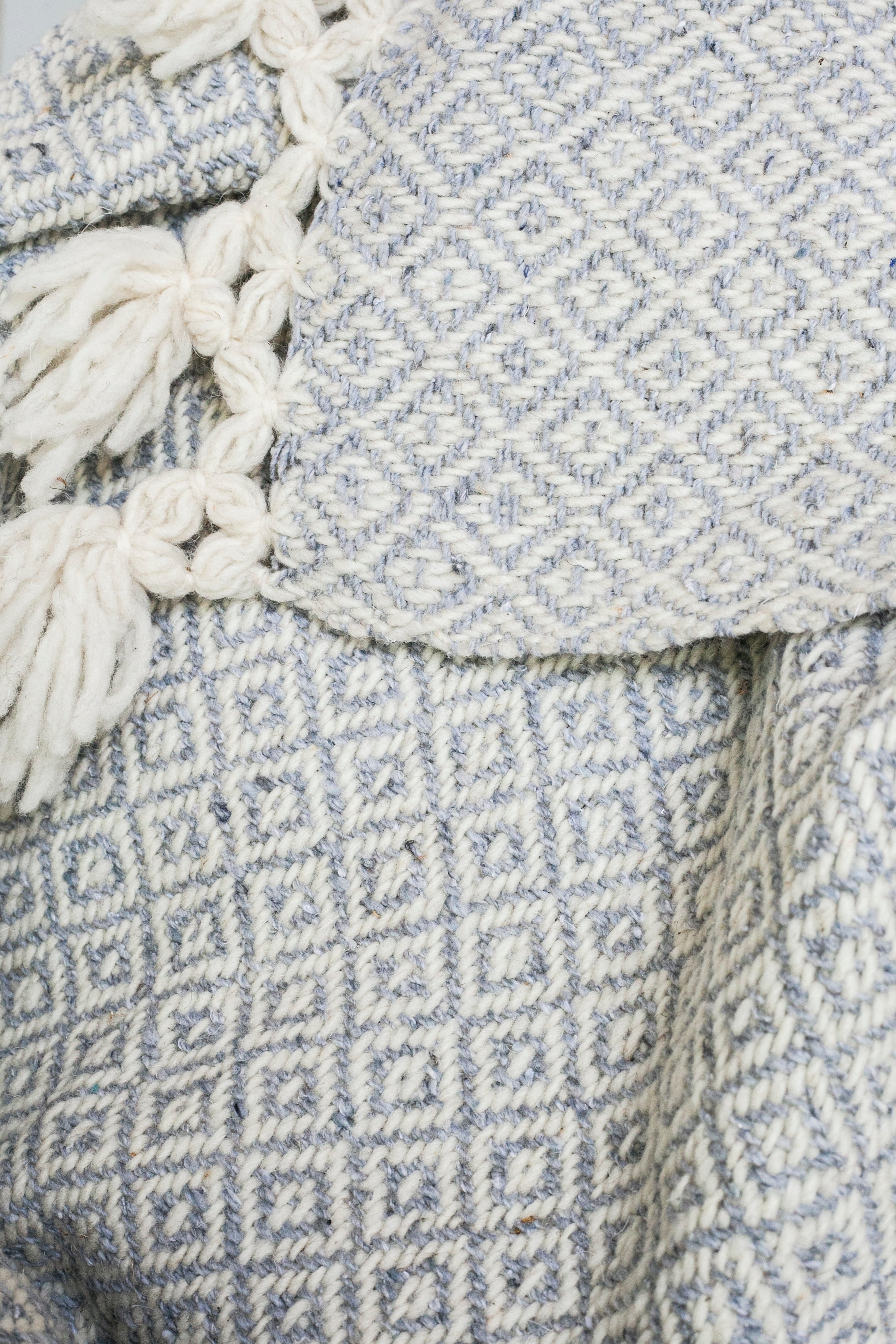 Detail of light grey and white diamond weaving and tied tassels from a wool throw blanket