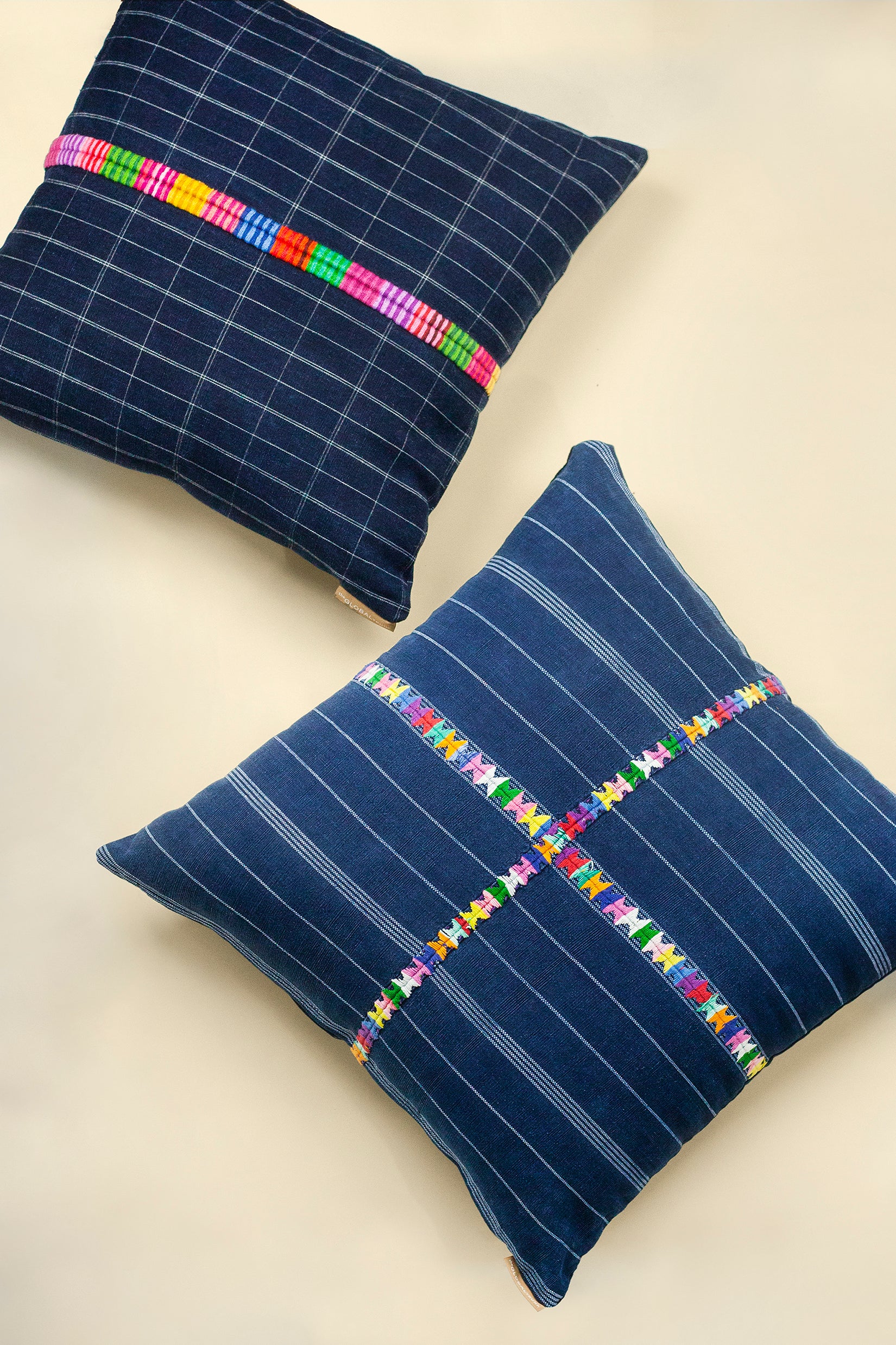 A pair of square pillows in different shades of navy with white geometric lines and a colorful geometric embroidered seam running across