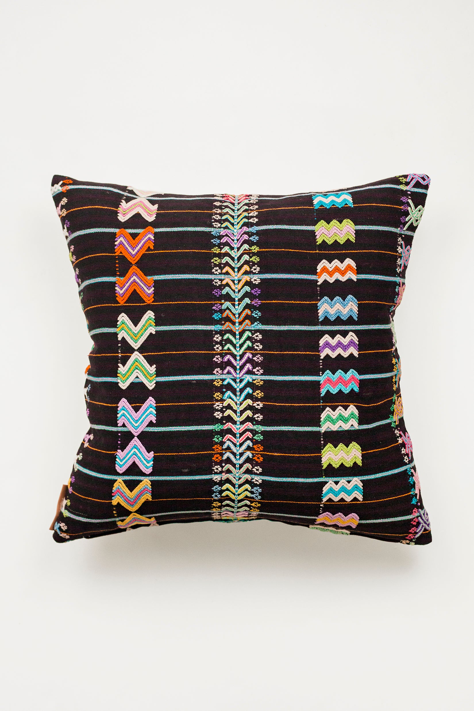 A square throw pillow with a striped brown burgundy textile and colorful hand embroidered brocade