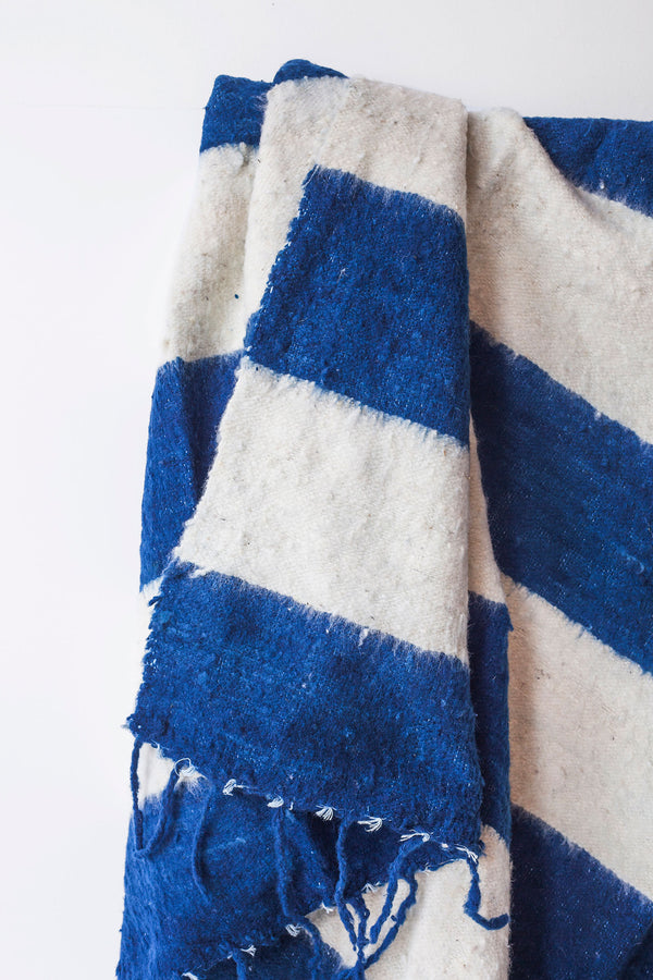 Detail of thick blue indigo stripes and tied tassels on queen size ecru wool blanket