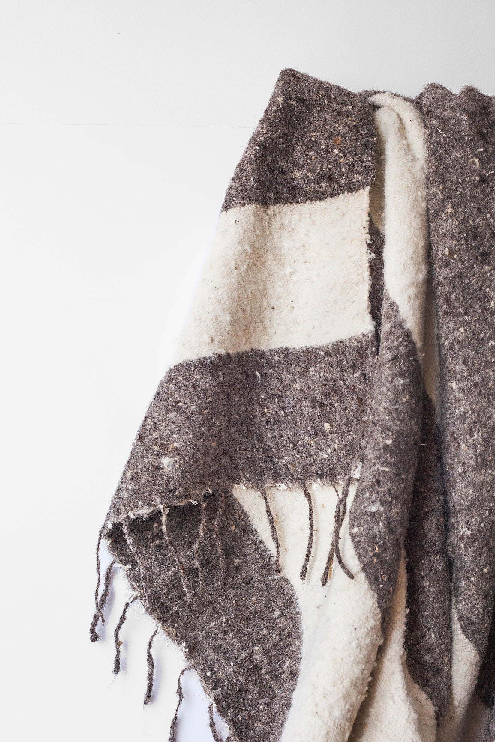 Detail of thick grey stripes and tied tassels on queen size ecru wool blanket