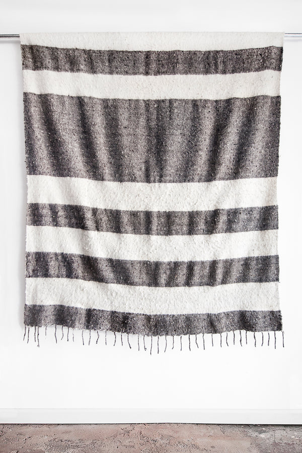 Queen sized ecru wool blanket with rows of thick horizontal grey stripes and a row of tied tassels at each end