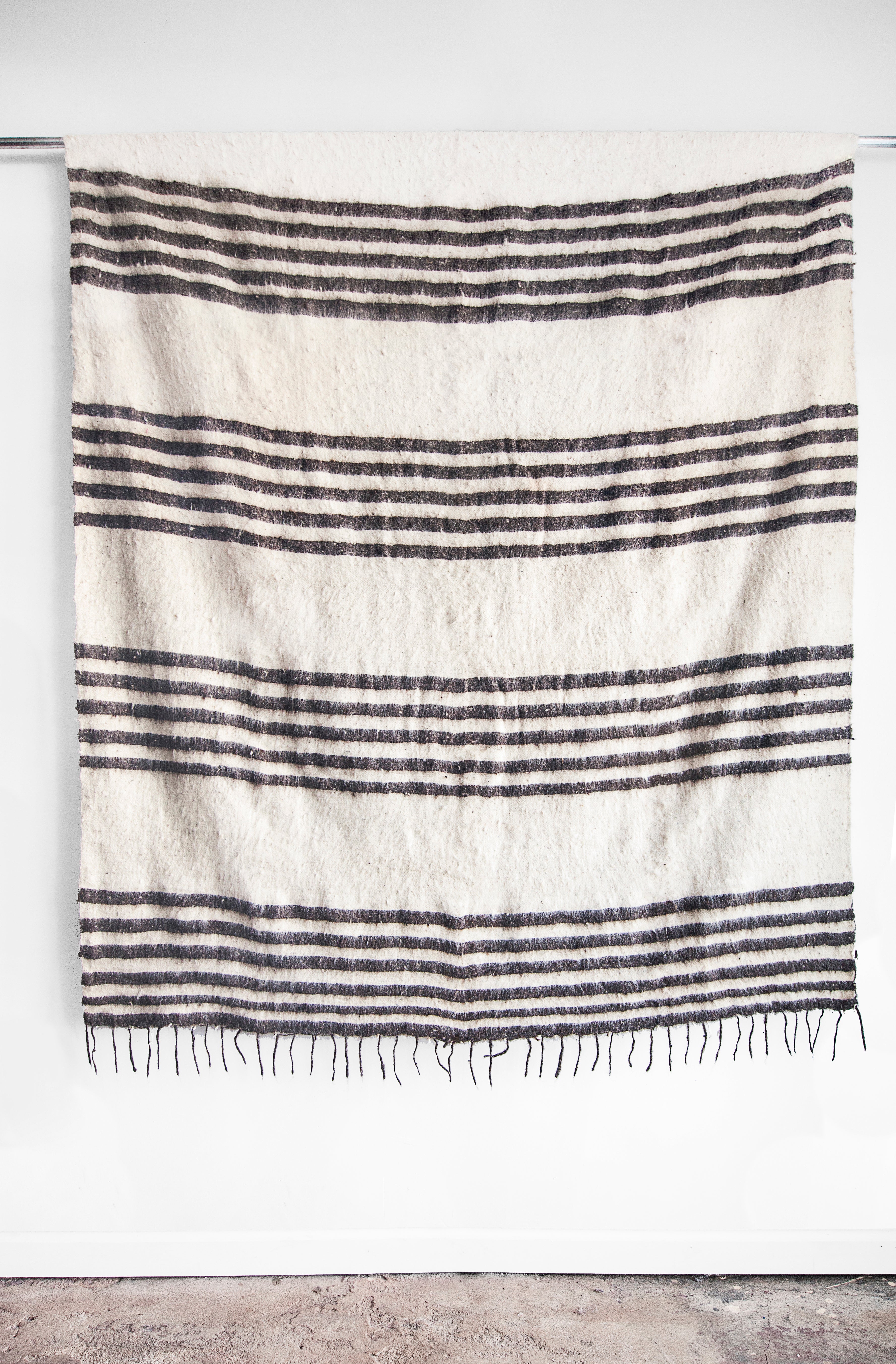 Queen sized ecru wool blanket with rows of horizontal grey stripes and a row of tied tassels at each end