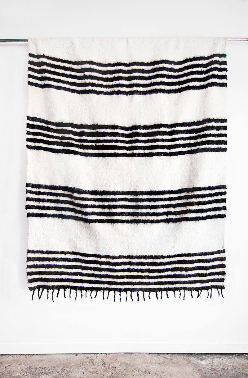 Queen sized ecru wool blanket with rows of horizontal black stripes and a row of tied tassels at each end