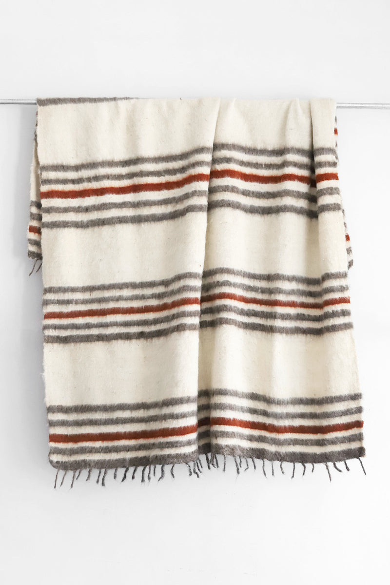 Queen sized off-white wool blanket with rows of horizontal grey and dark red stripes and a row of thin grey tied tassels at each end