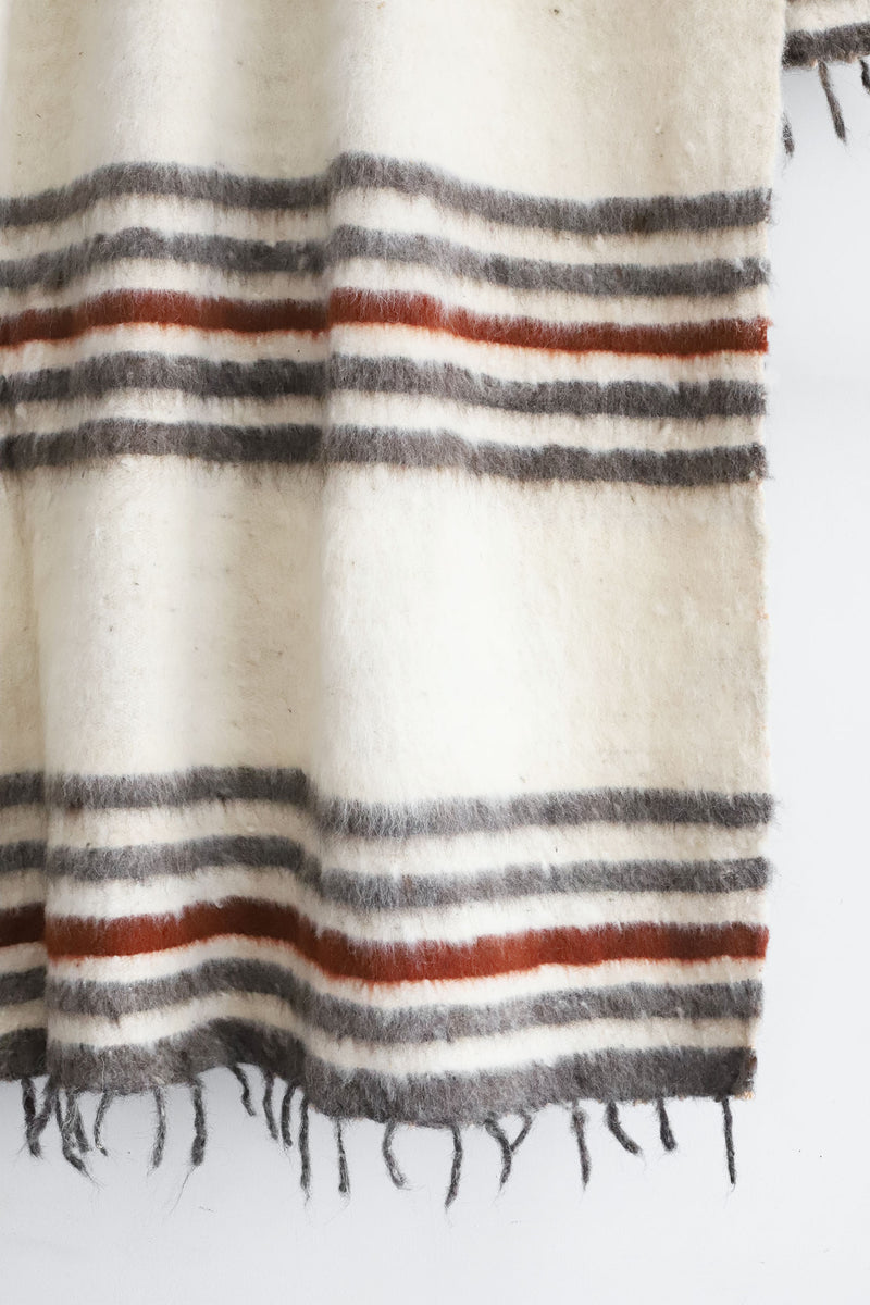 Detail of grey and dark red stripes and tied tassels on queen size off-white wool blanket