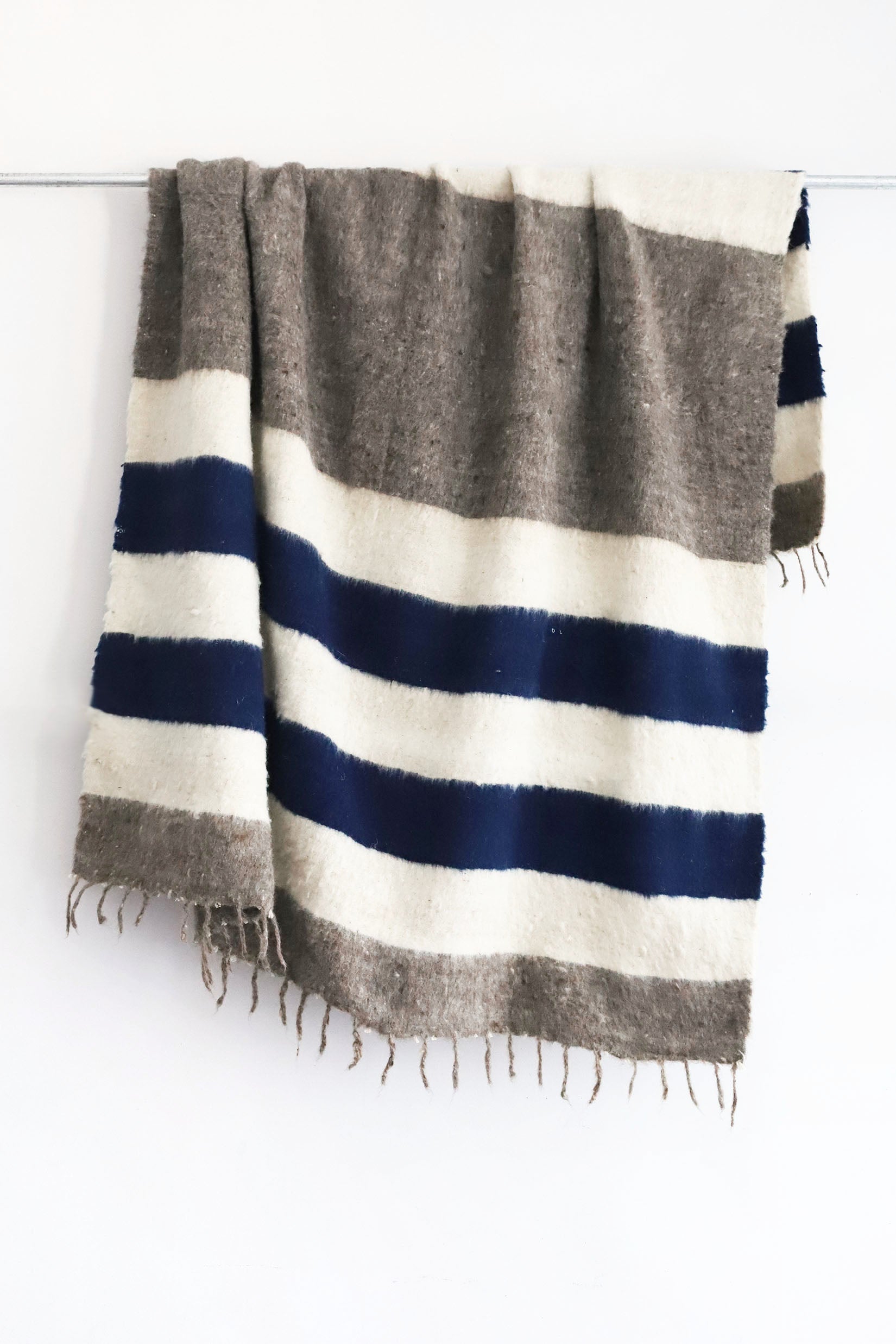 Queen sized ecru wool blanket with rows of thick horizontal blue indigo and grey stripes and a row of tied tassels at each end