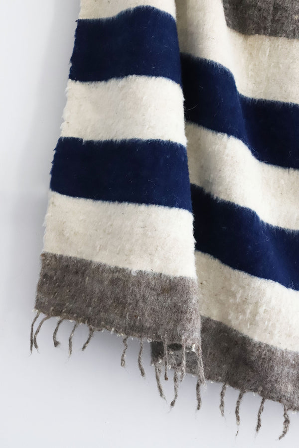 Detail of thick blue indigo and grey stripes and tied tassels on queen size ecru wool blanket