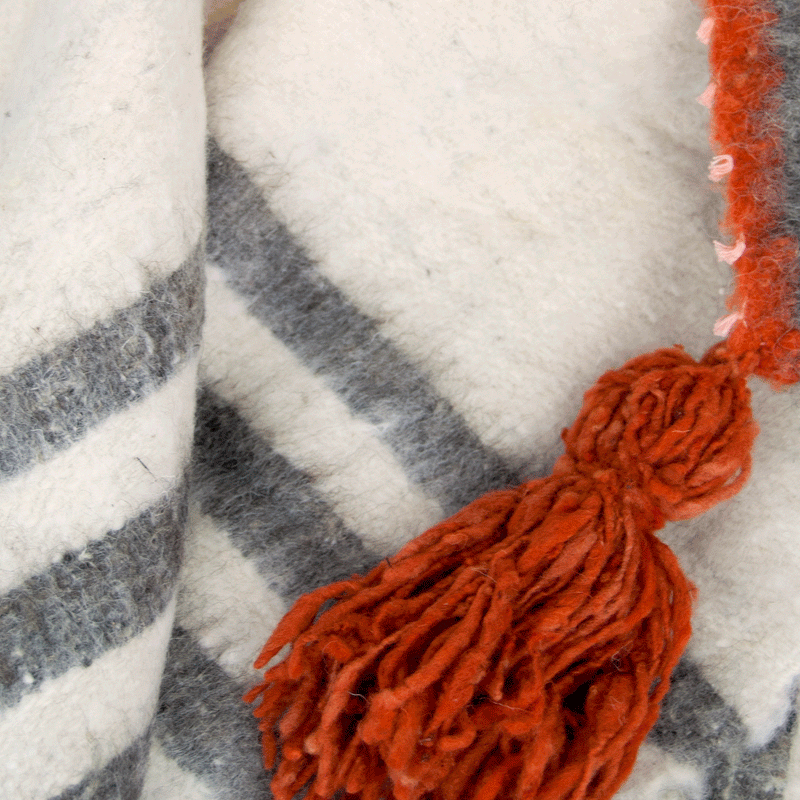 Detail of grey stripes and pumpkin tassel on queen size ecru wool blanket