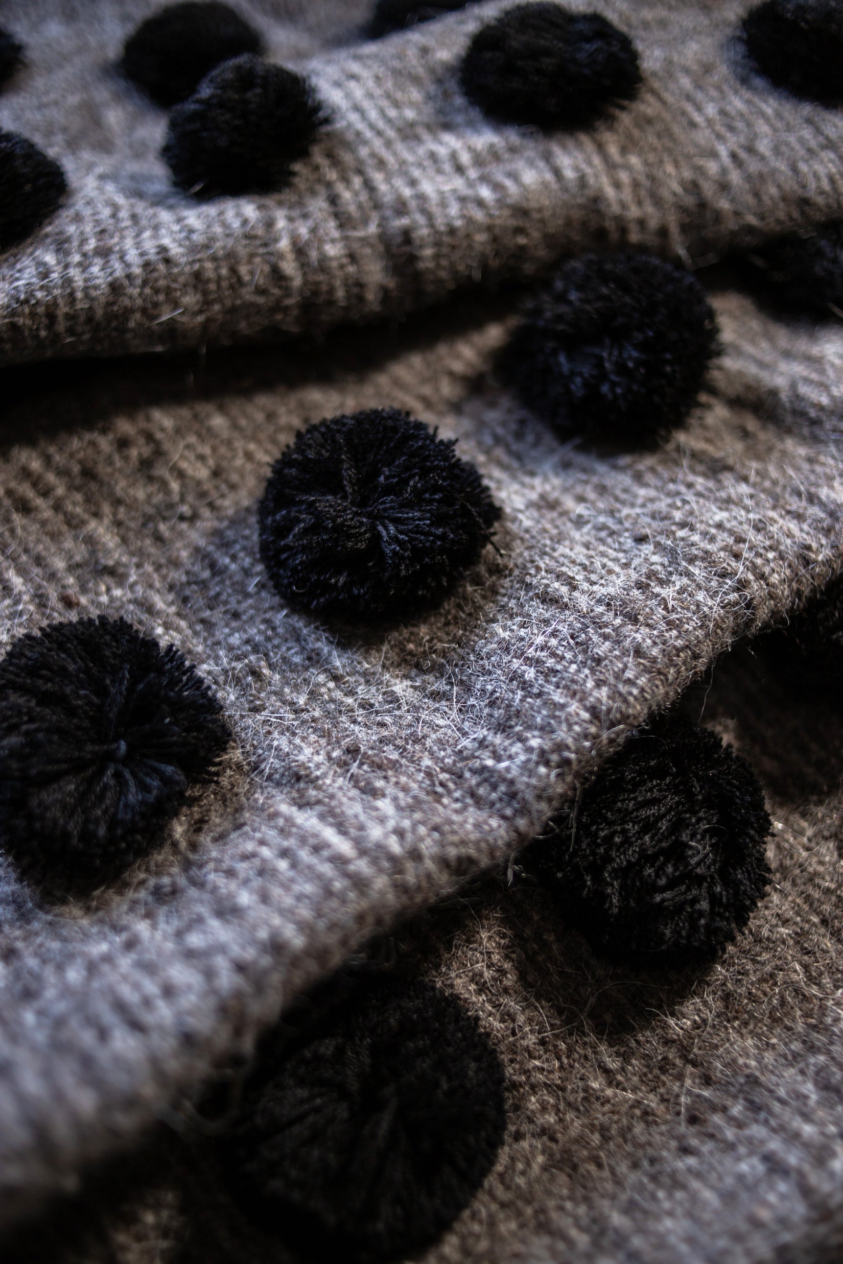 Grey wool throw covered in rows of black pom poms