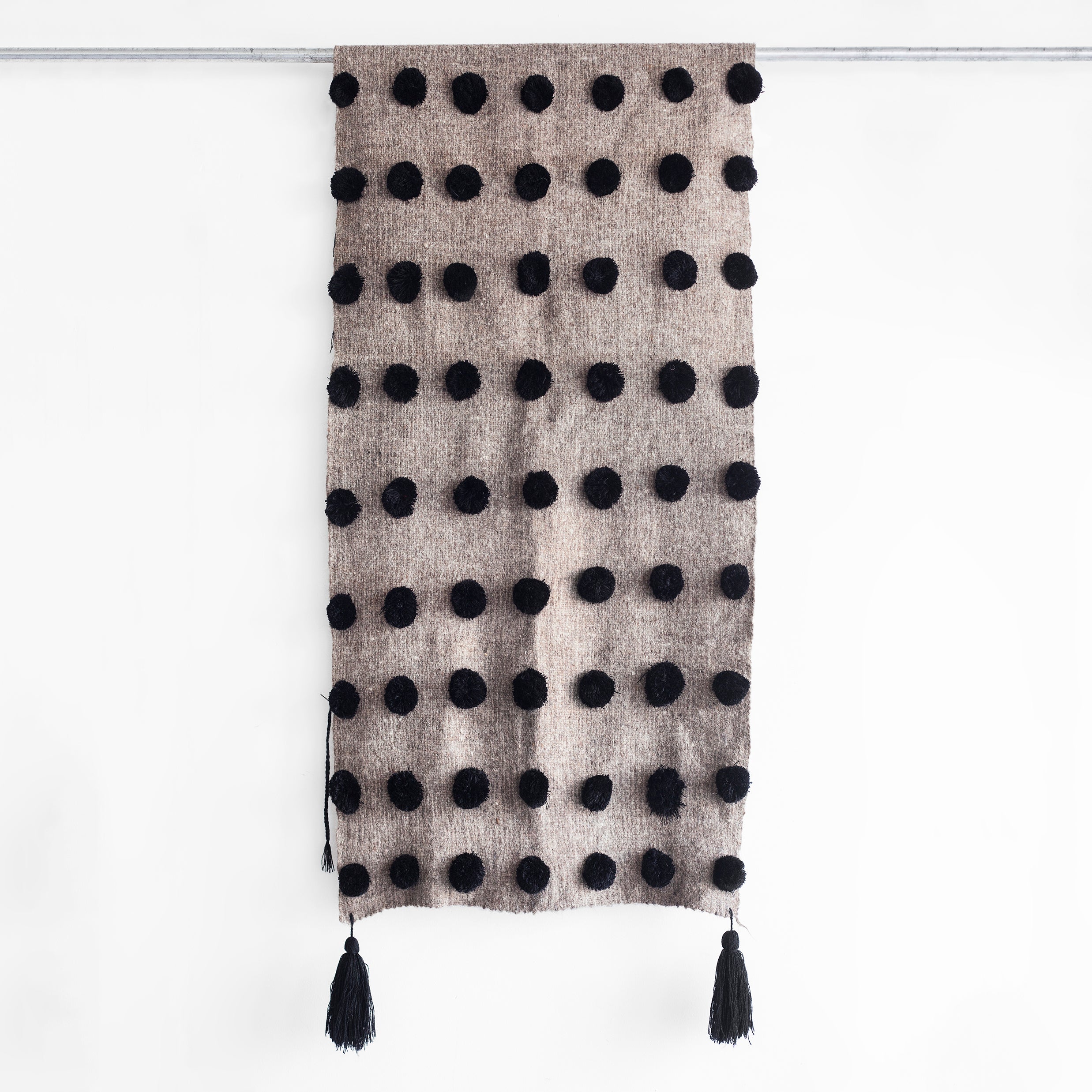 Grey wool throw covered in rows of black pom poms with black tassels at each corner
