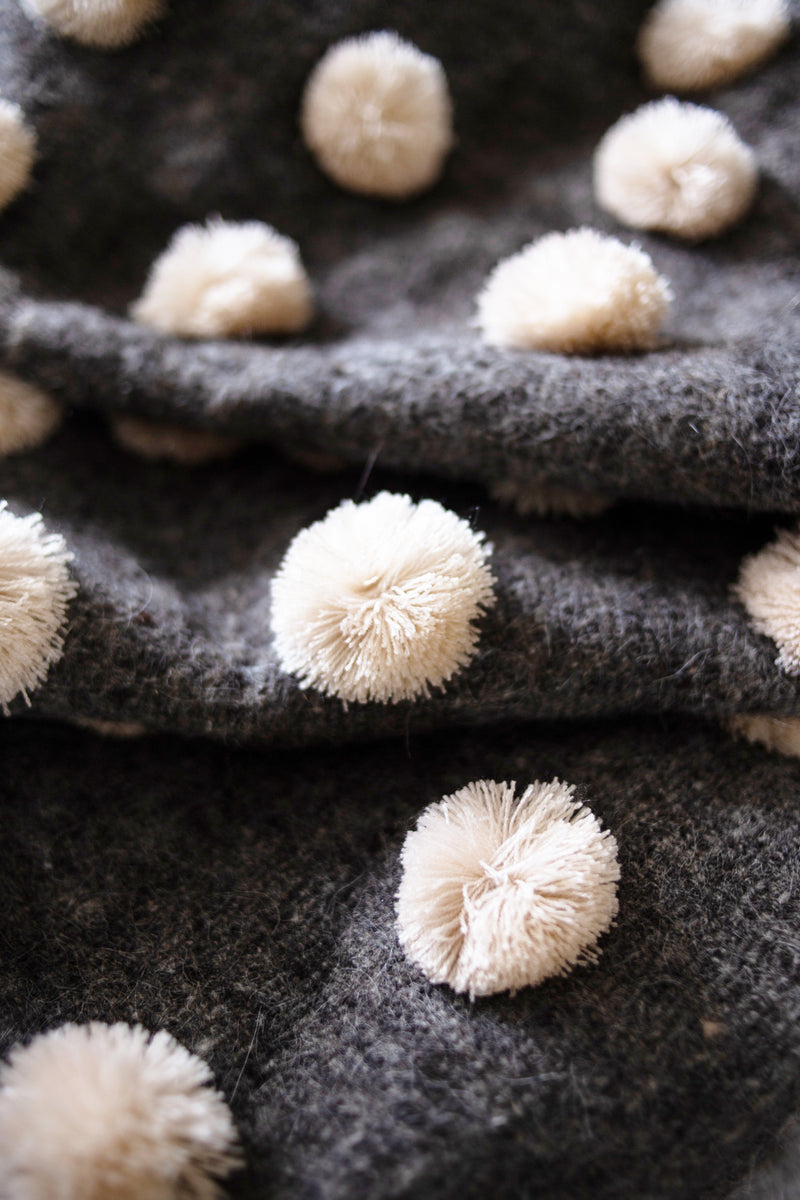 Detail of grey wool throw covered in rows of cream pom poms