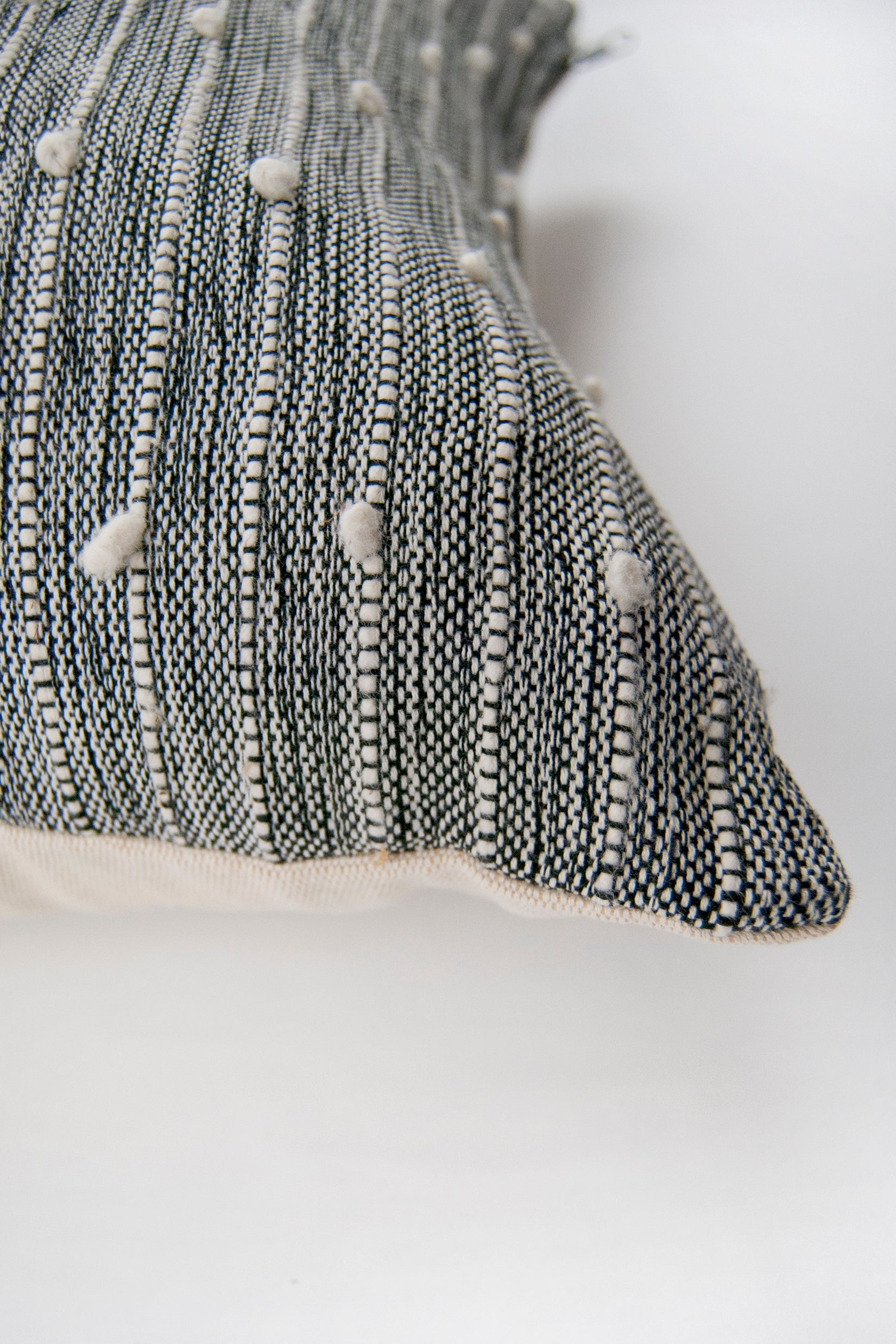 Corner detail of black and white woven throw pillow with small white pom pom accents