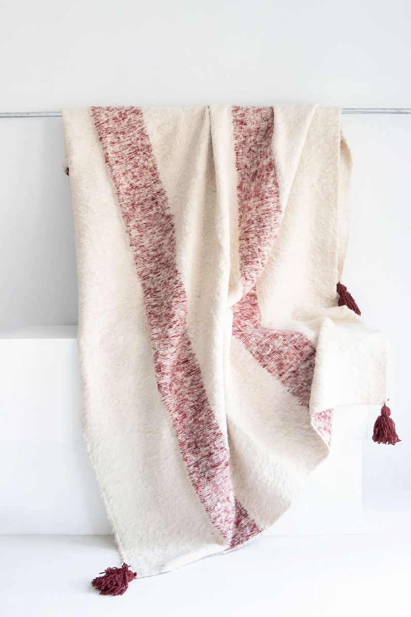 Queen size ecru wool blanket with two thick vertical burgundy stripes and burgundy tassels at each corner